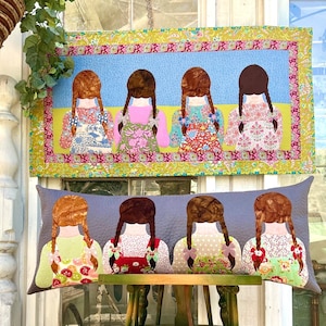 以下が含まれることがあります： グレーの背景に、花柄のドレスを着た女の子の刺繍が4つ施された長方形の枕。枕は黄色、緑、ピンクの縁取りで飾られています。