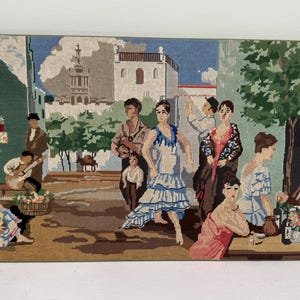 May include: A tapestry depicting a Spanish street scene with figures, including a flamenco dancer in a blue dress. The artwork features a guitarist, people at tables, and a building with a tower. The tapestry has gold tassels.