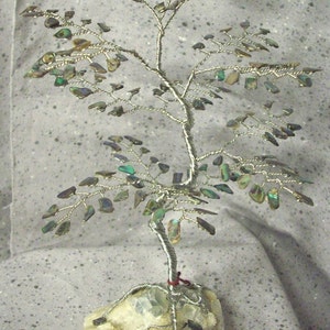 May include: A wire-wrapped tree sculpture with iridescent green leaves and a white crystal base.