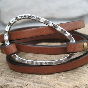 May include: A brown leather wrap bracelet with a silver, textured, oval-shaped clasp.
