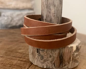 May include: A brown leather strap wrapped around a piece of driftwood. The strap is about 1 inch wide and is made of a soft, supple leather.