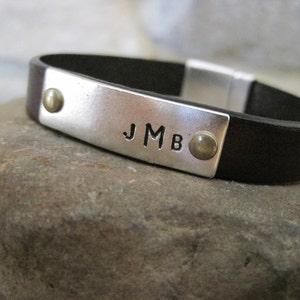 May include: A brown leather bracelet with a silver metal plate engraved with the initials "JMB".