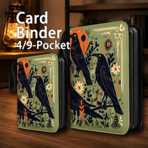 Könnte beinhalten: Zwei rechteckige Kartenordner mit schwarzen Reißverschlusskanten und einem salbeigrünen Einband mit einer grafischen Illustration von schwarzen Krähen, orangefarbenen Sonnen und weißen Blumen. Der Text Card Binder 4/9-Pocket ist in Weiß aufgedruckt.