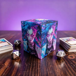 Op de afbeelding: Een kubusvormige kaartenopbergdoos met een levendige illustratie van een personage met blauw en roze haar en paarse ogen. Zilveren dobbelstenen en stapels kaarten zijn gerangschikt op een houten oppervlak, met een paarse achtergrond.