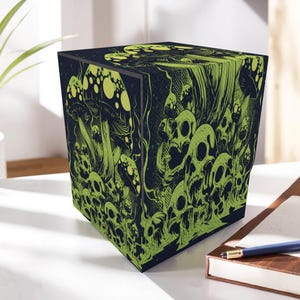 May include: A cube-shaped storage box with a dark blue background and a neon green illustration of skulls and mushrooms. The box is sitting on a white surface next to a notebook and pen.