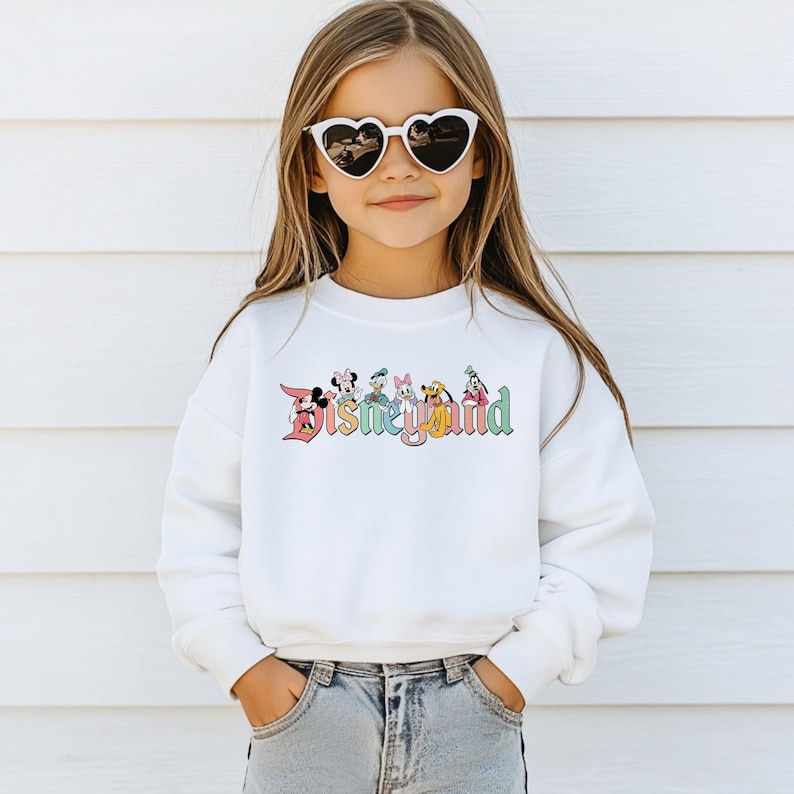 May include: White sweatshirt with a colorful Disney Land graphic featuring Mickey Mouse, Donald Duck, Minnie Mouse, Goofy, Pluto, and Daisy Duck.