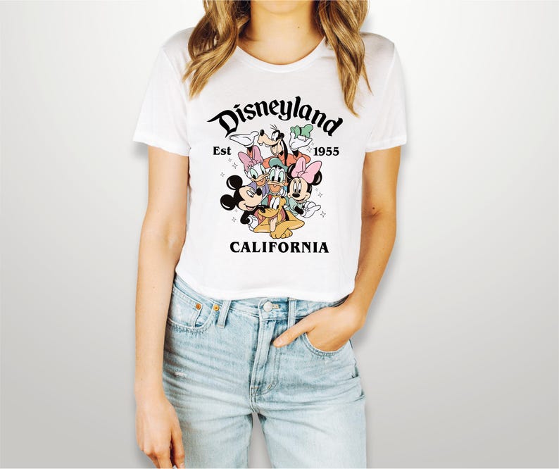 May include: White t-shirt with a graphic of Mickey Mouse, Minnie Mouse, Donald Duck, Goofy, and Pluto. The graphic is surrounded by the text "Disneyland Est 1955 California".