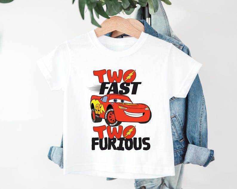 Peut inclure: T-shirt blanc avec une voiture de course rouge de dessin anim&eacute; et le texte "TWO FAST TWO FURIOUS" en rouge et noir. Le design comprend des &eacute;clairs. Un t-shirt color&eacute; pour enfants.