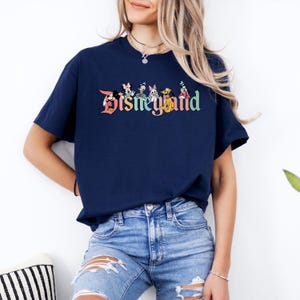 May include: A navy blue t-shirt with a colorful Disney World logo featuring Mickey Mouse, Minnie Mouse, Donald Duck, Daisy Duck, Goofy, and Pluto. The logo is in a vintage style with a rainbow color scheme.