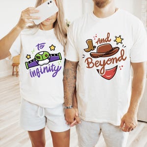 Puede incluir: Dos camisetas blancas con diseños a juego. Una presenta un diseño de nave espacial de dibujos animados con el texto "to infinity" en morado. La otra camiseta tiene un sombrero de vaquero, una bota y las palabras "and beyond" en marrón.