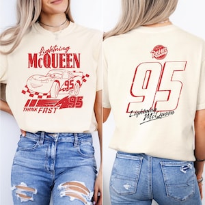 Może przedstawiać: Biała koszulka z czerwonym nadrukiem Błyskawicy McQueena z filmu Auta. Z przodu koszulka ma napis "Lightning McQueen" i "Think Fast". Z tyłu koszulka ma numer "95" i napis "Lightning McQueen" w kolorze czerwonym.