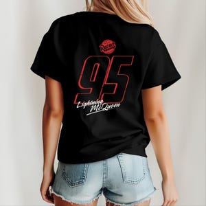 Może przedstawiać: Czarny T-shirt z czerwoną liczbą 95 i tekstem "Lightning McQueen" oraz czerwonym k&oacute;łkiem z tekstem "Rust-eze" z tyłu.
