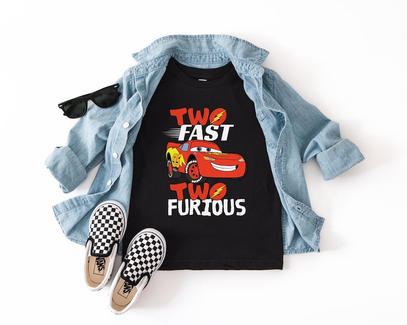 Peut inclure: Un t-shirt noir avec l'inscription "TWO FAST TWO FURIOUS" et un dessin de voiture de course rouge. L'ensemble comprend une veste en jean bleu clair, des lunettes de soleil noires et des baskets &agrave; enfiler &agrave; carreaux noirs et blancs.