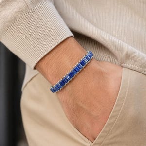 May include: A bracelet featuring a series of square-cut, deep blue lapis lazuli stones set within a silver-toned metal chain. The stones are arranged in a single row, alternating with small metallic links, creating a structured and uniform appearance.