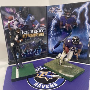 May include: Two framed photos of Baltimore Ravens football players, one of Rick Henry with the text "1000 Career Rushing Yards" and the other of a player wearing number 22. The photos are on a purple mat with a Baltimore Ravens logo.
