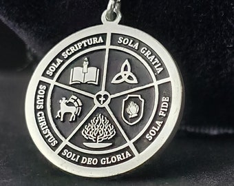 May include: A silver pendant necklace with a round black disc featuring the five solas of the Reformation: Sola Scriptura, Sola Gratia, Sola Fide, Solus Christus, Soli Deo Gloria. The disc is surrounded by a silver border.