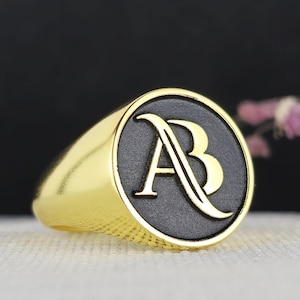 May include: A gold signet ring with a black oval top featuring the letters "AB" in gold.