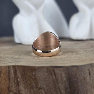 May include: A rose gold ring with a smooth, polished band. The interior of the ring is clearly engraved with the text 10K, indicating the gold purity. The ring is positioned to show the inner band and the hallmark stamp on the metal surface.