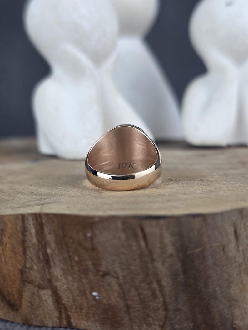May include: A rose gold ring with a smooth, polished band. The interior of the ring is clearly engraved with the text 10K, indicating the gold purity. The ring is positioned to show the inner band and the hallmark stamp on the metal surface.