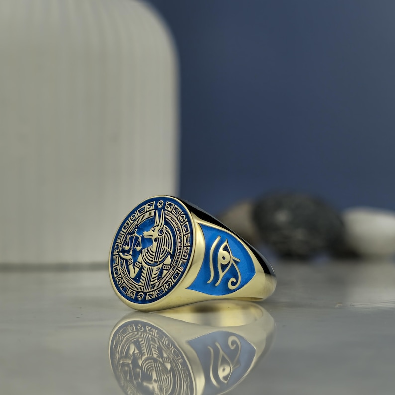 This handmade Anubis ring offers a glimpse into ancient Egyptian spirituality, with symbols reflecting balance, justice, and the sacred journey of the soul. Finished with gold plating and blue enamel, its face showcases the Egyptian jackal-headed deity in ceremonial regalia. Crafted with care and precision, it's perfect for mythology lovers or collectors of symbolic jewelry with deep cultural significance.