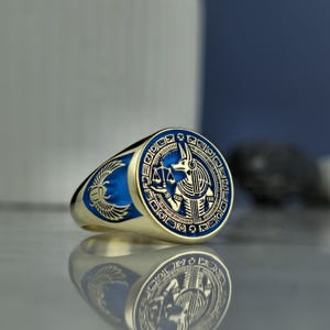 Elevate your jewelry collection with this handcrafted Anubis signet ring, inspired by the ancient Egyptian deity known for guiding souls to the afterlife. The fine gold plating and deep blue enamel add a modern touch to its mythological roots. Each detail of the design—from the weighing scale to the hieroglyphic border—celebrates Anubis’s iconic role in judgment and protection. A meaningful gift for those drawn to ancient lore, spirituality, and regal aesthetics.