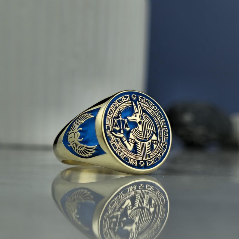 This exquisite Anubis ring merges ancient Egyptian symbolism with modern craftsmanship, featuring a rich blue enamel and meticulously engraved Anubis figure. Designed for those who appreciate spiritual heritage and unique design, this piece is handcrafted from 925 sterling silver and gold-plated to perfection. With its polished surface and bold mythological presence, it reflects timeless elegance and mystery.