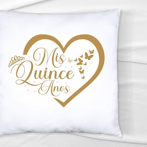 Op de afbeelding: Wit kussen met een gouden hartvormig ontwerp met de tekst "Mis Quince Anos" en gouden vlinders rond het hart.