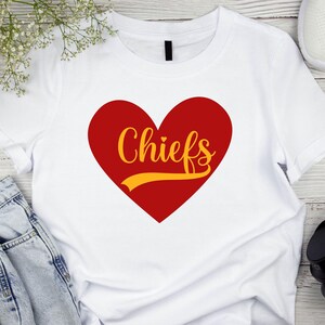 May include: White t-shirt with a red heart and the word "Chiefs" in yellow lettering.