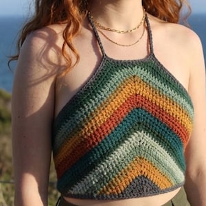 Peut inclure: Haut crochet fait à la main, de style dos nu, avec un motif en chevrons. Le haut présente une palette de couleurs vertes, teal, orange, jaune et grise. Le haut est de style crop top et a un col halter.