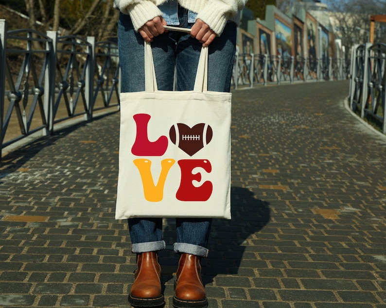 May include: White tote bag with the word "LOVE" in red, yellow, and brown letters. A brown football in a heart shape is above the "O".