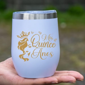 Op de afbeelding: Een witte roestvrijstalen tumbler met een gouden ontwerp met de tekst "Mis Quince Anos" en een kroon met een vrouwenhoofd.