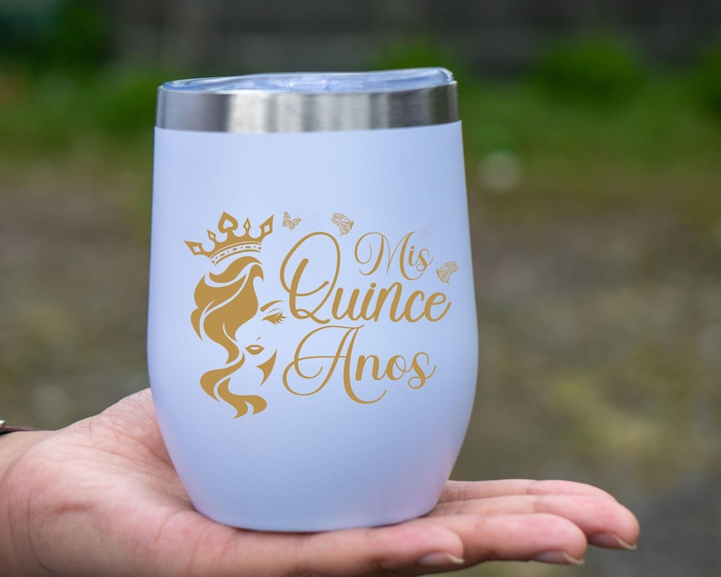 Op de afbeelding: Een witte roestvrijstalen tumbler met een gouden ontwerp met de tekst "Mis Quince Anos" en een kroon met een vrouwenhoofd.