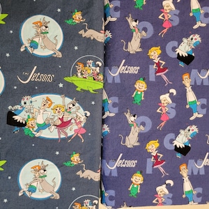 May include: Two fabric swatches with a repeating pattern of The Jetsons characters. The fabric on the left is dark blue with white stars. The fabric on the right is purple with white stars. Both fabrics feature the text "The Jetsons" and various characters from the cartoon.