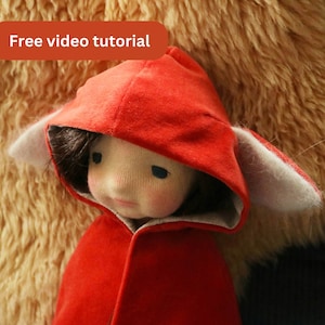 May include: A red hooded doll with a white fur trim around the hood and ears. The doll has a light brown wig and a painted face.