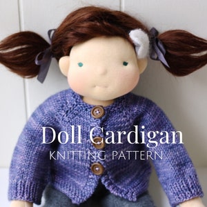 May include: A purple knitted doll cardigan with brown buttons. The text "Doll Cardigan Knitting Pattern" is printed below the doll.