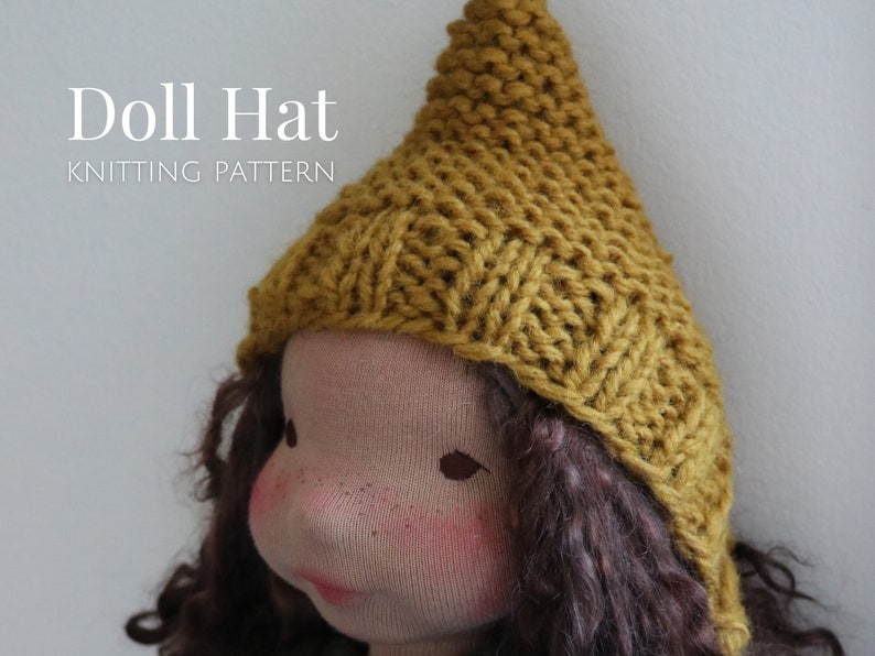 K&ouml;nnte beinhalten: Eine gestrickte Puppenm&uuml;tze in senfgelber Farbe. Die M&uuml;tze ist mit einem einfachen Stichmuster gearbeitet und hat eine spitze Krone.