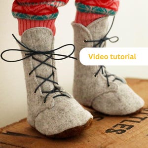 May include: Gray felt boots with black laces tied in a bow. The boots have a brown sole and are worn by a doll with red and green patterned socks.
