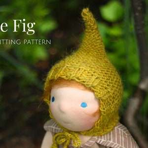 K&ouml;nnte beinhalten: Eine Puppe tr&auml;gt eine gelbe Strickm&uuml;tze mit einer spitzen Spitze. Die M&uuml;tze hat eine Strickstruktur und hei&szlig;t "Le Fig" Strickmuster.