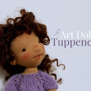 May include: A brown-skinned art doll with curly brown hair wearing a purple knitted sweater. The doll is looking up and has a sweet expression. The text "Art Doll Tuppence Step by Step Pattern" is in the background.