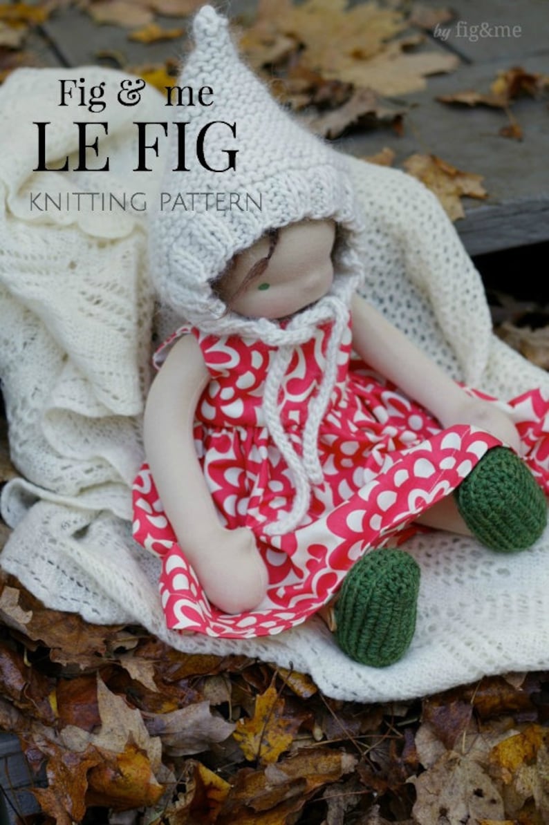 K&ouml;nnte beinhalten: Eine gestrickte Puppe, die einen wei&szlig;en H&auml;kelhut und ein rot-wei&szlig;es Blumenkleid tr&auml;gt. Die Puppe sitzt auf einer wei&szlig;en H&auml;keldecke mit braunen Bl&auml;ttern im Hintergrund. Der Text "Fig & me LE FIG KNITTING PATTERN" ist im Bild sichtbar.