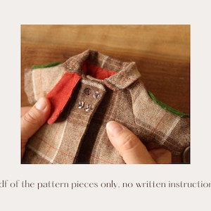 May include: A brown and tan plaid fabric jacket with a red collar and green trim. The jacket has a button closure and is being held by a hand.