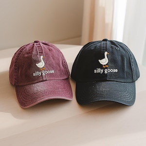 May include: Two baseball caps with a white goose and the text "silly goose" embroidered on the front. One cap is burgundy and the other is black.