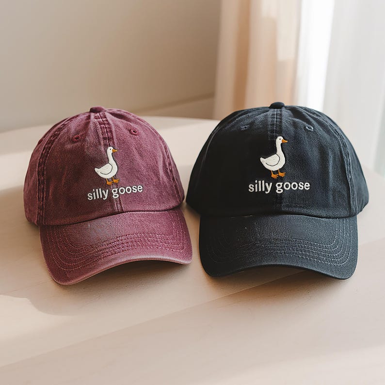 May include: Two baseball caps with a white goose and the text "silly goose" embroidered on the front. One cap is burgundy and the other is black.