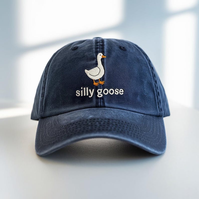 May include: A dark blue denim baseball cap with an embroidered white goose and the text "silly goose" in white.