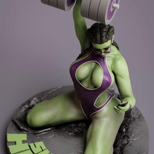 May include: A green She-Hulk figurine lifting a dumbbell. She wears a purple swimsuit and glasses. The base features the words "SHE HULK" in green.