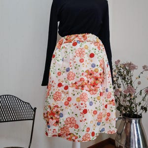 May include: A black long-sleeved turtleneck top paired with a white skirt adorned with a vibrant floral pattern in red, orange, and blue. The skirt is pleated and falls to the knees, creating a classic silhouette.