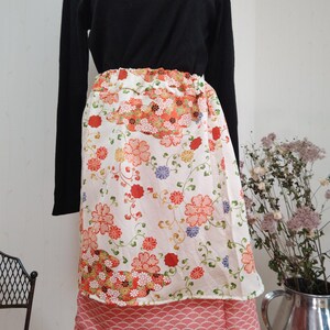 Puede incluir: Una falda blanca de envolver con estampado floral en tonos rojos, naranjas y azules. La falda tiene una capa inferior rosa con un patrón de ondas.