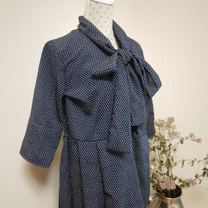 May include: A navy blue dress with a white polka dot pattern. The dress has a bow tie at the neck and three-quarter sleeves.