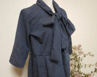May include: A navy blue dress with a white polka dot pattern. The dress has a bow tie at the neck and three-quarter sleeves.