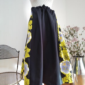 May include: A black maxi skirt with a yellow and blue floral print on the sides. The skirt has a gathered waistband and a flowing silhouette.